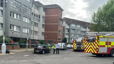 A block of flats taped off with police officers and fire engines behind the cordon