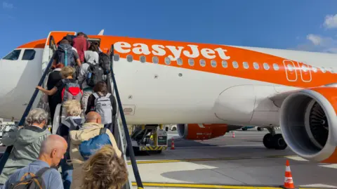 Getty Images Passengers walking up a set of stairs to board an EasyJet plane