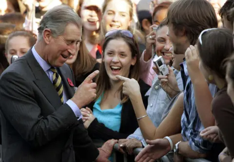 AP Charles laughs and chats with students. He points a finger at one student, as they take his photo