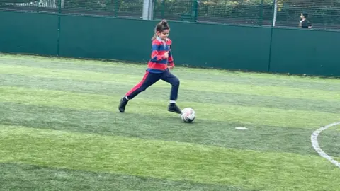 Family handout Talvin runs, kicking a football on an astroturf pitch. He is the only person on the court that we can see. and wears a striped blue and red rugby top and matching joggers. 