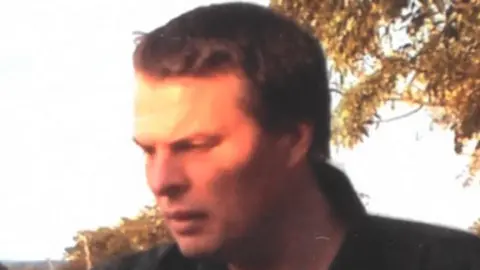 Darren Round pictured with brown hair wearing a blue and white stripe collar T-shirt and dark jacket.