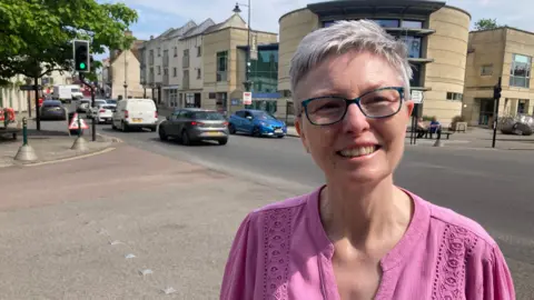 Eugene Gooch looks into the camera, wearing glasses and pink top while standing in Calne town centre.