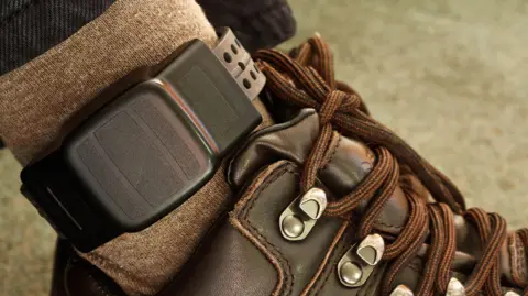 Getty Images File image showing a black electronic GPS tag fitted around a person's ankle. Their brown socks and brown lace-up boots are visible