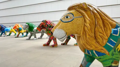 A line of lions arranged in a semi-circle, all of which are covered with very bright colourful designs.