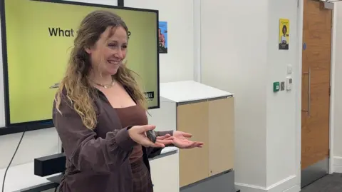 Laura Poole Laura wearing a brown suit jacket and matching brown checkered smart trousers.