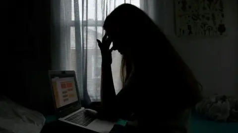 Getty Images A girl looks sadly at her laptop. She is silhouetted to highlight the despair felt by those in this situation. 