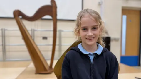 A young girl wearing school uniform smiles at the camera