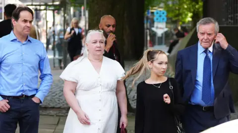 PA Media Paula Leeson's brother Neville Leeson (left) and father Willy Leeson (right) outside Manchester Civil Justice Centre along with other family members.