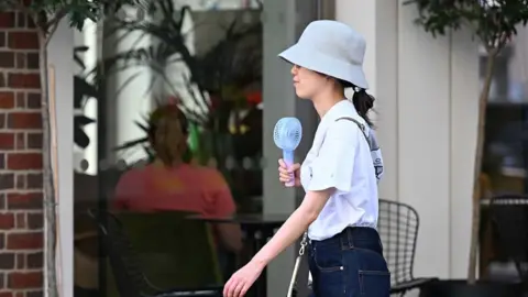 Woman holding fan and wearing hat on a London street