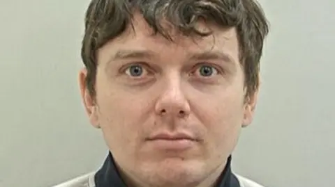 A mugshot of Andrew Sullivan, who has tousled brown hair and is clean shaven.