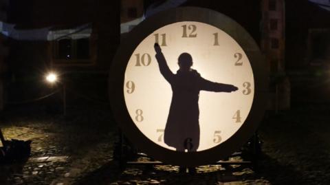 A figure in front of an illuminated clock