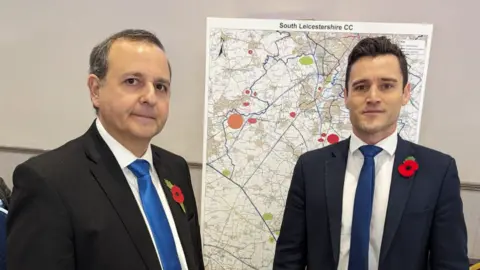 Alberto Costa Two men in suits and ties. Neither looks happy