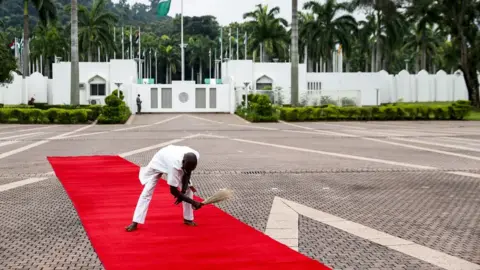 EPA An employee brooms the red carpet ahead of the arrival of German Chancellor Angela Merkel to her meeting with the President of Nigeria at the State House, in Abuja, Nigeria, 31 August 2018.