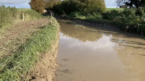 A country road with a large flood and very muddy banks.