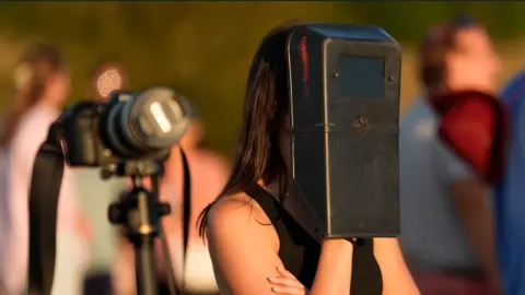 PA Media A woman is wearing a black welding mask looking at the sun