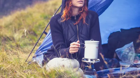 Woman sits in tend heating pot on camping stove