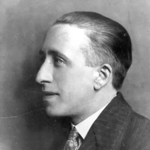 Lewis Grassic Gibbon in profile in black and white. He is wearing a dark pin-striped suit and a shirt and patterned tie. He is smiling slightly.