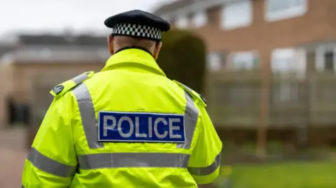 Getty Images A photo of a police officer from behind. They are wearing a high-vis jacket which reads Police. 