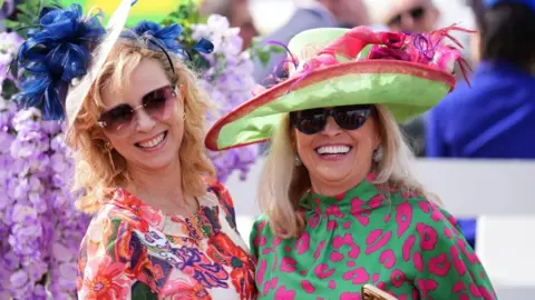 PA Media A woman in dressed in a multi-coloured floral dress with a woman in a green and pink leopard print dress