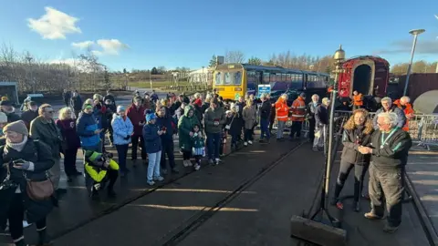 Dozens of people, including photographers and children, pictured in front of historic trains