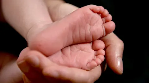 PA Media A person holding a baby's feet.