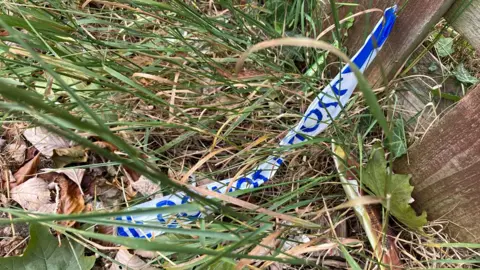 Jenny Kirk/BBC Police tape in undergrowth