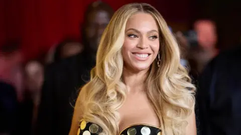 Beyonce has long blonde hair and a strapless gold and black spotted dress