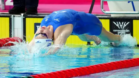 PA Media Katie Shanahan, wearing a blue swimming costume, dives into the pool during a race at the Commonwealth Games.