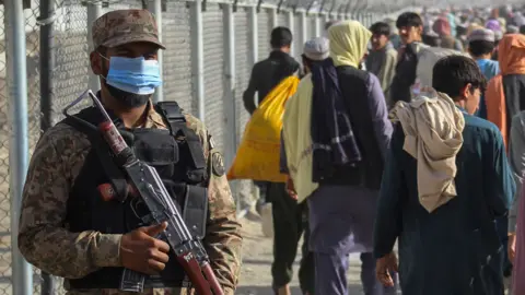 AFP A Pakistani soldier stands guard as Afghans walk along fences after arriving in Pakistan through the Pakistan-Afghanistan border crossing point in Chaman on 26 August 2021