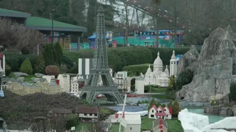 A Lego Eiffel Tower can be seen surrounded by other French monuments made from the toy bricks in the park which is full of hedges and trees.