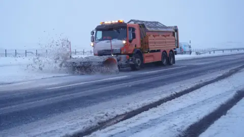 PA Media An orange snow plough clears the road on the A66 in Durham, north east England. Yellow weather warnings for snow and ice remain in force across parts of the UK.