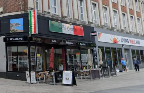 Google The front entrance of Caffe Caruso with tables outside and an Italian flag sign over the front door