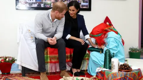 Getty Images The Duchess of Sussex sits with Prince Harry as henna is applied to her hand