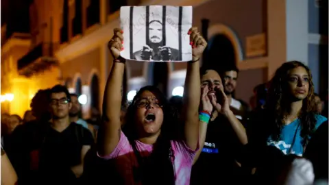 Getty Images A protestor carrying a sign that reads Ricky resign