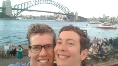 OLIVIA HOGARTH Olivia Hogarth and her partner smiling in front of the Sydney Harbour Bridge
