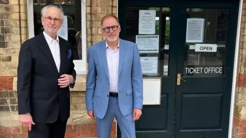 Liberal Democrats Two men wearing suits standing next to a ticket office