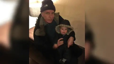 Sam Grace Chris Grace with his grandson wearing coats indoors