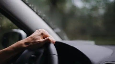 Getty Images A person's hand on a steering wheel