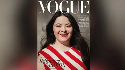 Vogue Ellie on the front of Vogue magazine. She is wearing a red and white striped top. She has long brown hair and is smiling. 