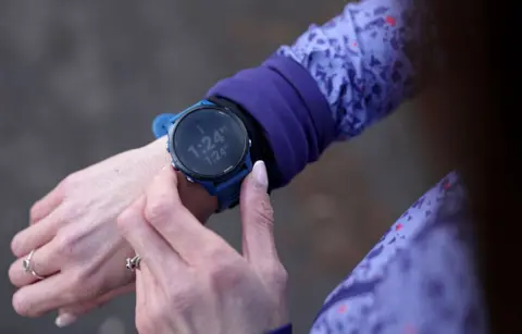 Kristian Johnson/BBC A close-up of a woman checking her smart watch by pressing buttons and looking at statistics showing up on the screen.