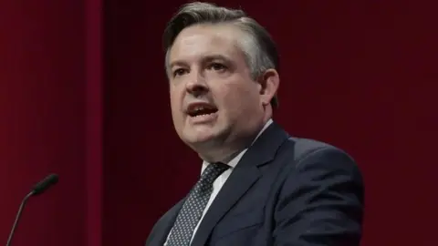 BBC A man in a suit at a lectern giving a speech.