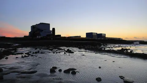 Hinkley Point A and B are seen by the coast with a sunset behind them.