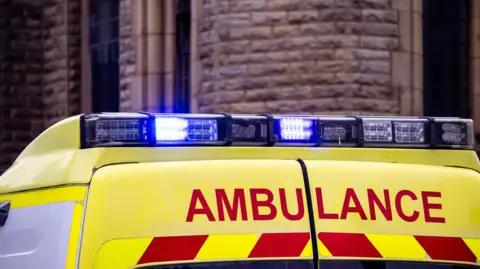 A stock photo of an ambulance with blue lights flashing.