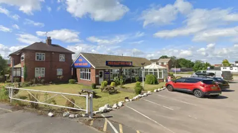 Google General view of the Salt Box cafe. It has some landscaping at the front along with some parked cares. 