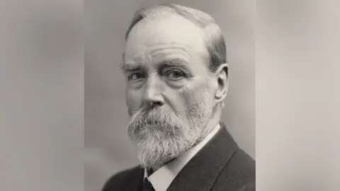 Judith Merrill Black and white archive image of architect AF Scott. He is wearing a dark suit jacket and light shirt. His white hair is neatly parted and he has a well-trimmed beard. 