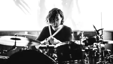 Rebecca Cleal Scalping/Scaler performing - Black and white image of a man drumming 
