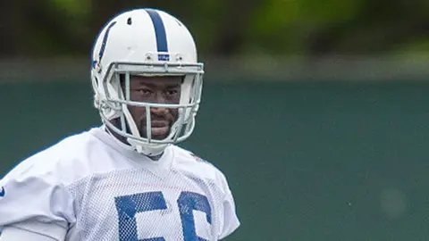 He is wearing his American football uniform, but the image is cut just below his shoulders. He is wearing a white helmet with a blue stripe down the middle and a white tshirt with blue detailing