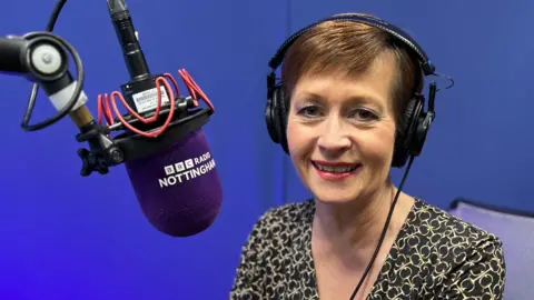 Sara Blizzard wearing black headphones and sat in front of a purple-headed microphone