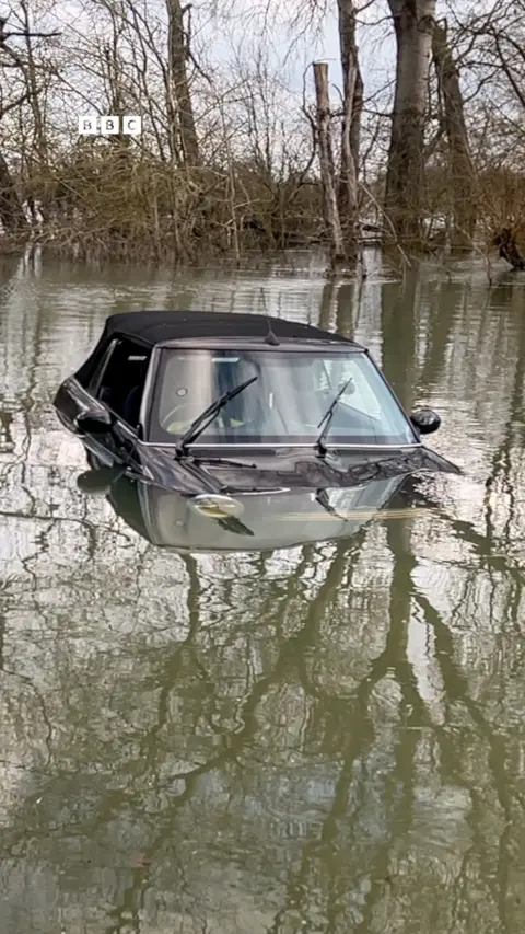A partially submerged Mini car in a flooded river