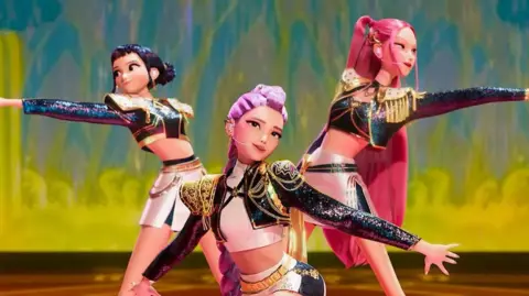 Netflix/ Sony Pictures Animation Picture of the animated band HUNTR/X, which is made up of performers Ejae, Audrey Nuna and Rei Ami who appear as cartoon characters in matching bolero jackets, A-Line skirts and an assortment of colourful wigs in pink and purple. 